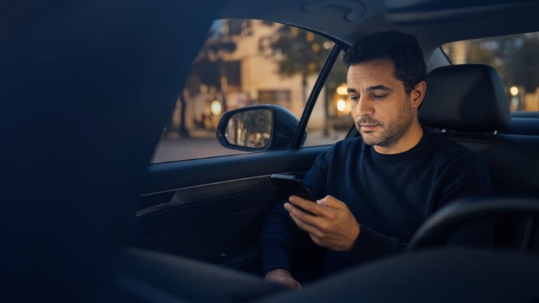 Chauffeur VTC au volant de sa berline vérifiant son contrat d'assurance sur son smartphone après la décision de l'ACPR concernant Wakam